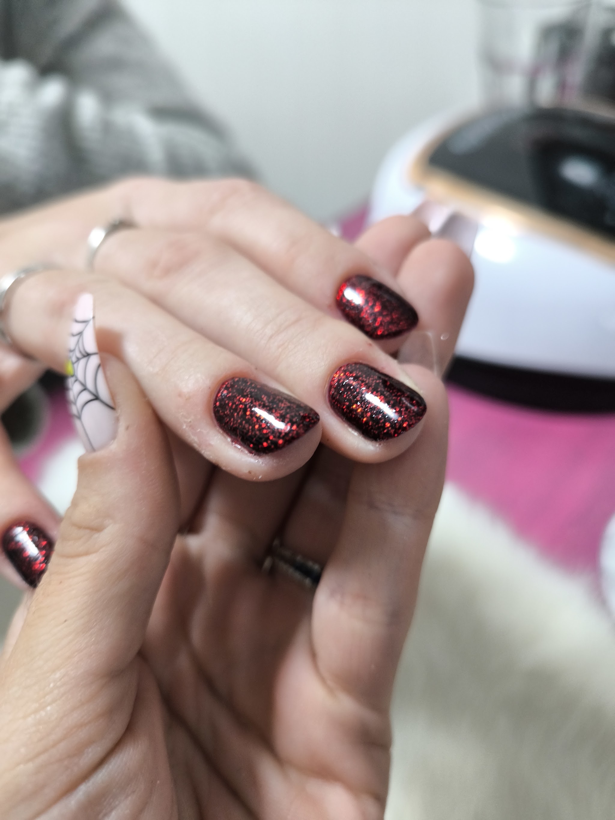 Rode glitternagels met een spinnenweb-accent, nagellamp op de achtergrond